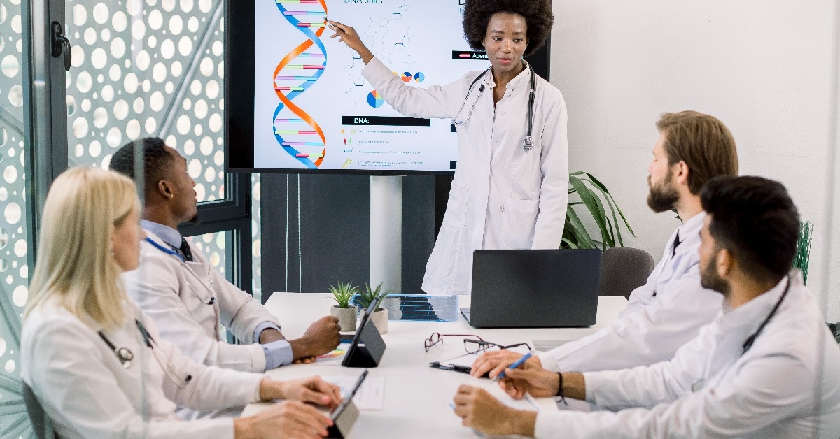 Professional young African female doctor talking to her multiracial team of colleagues about human DNA suffering from genetic disease.