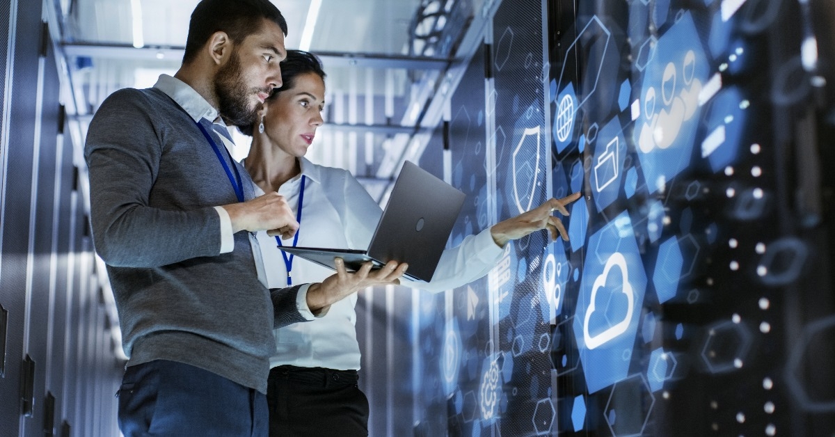 Male IT specialist holding laptop and discussing work with female server technician while Standing in Data Center 