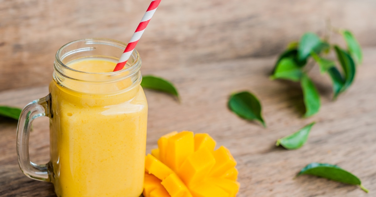 A delicious mango smoothie is served in a glass mason jar with a red-striped straw, set against an old wooden background.
