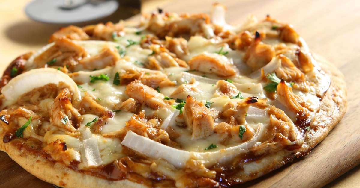 A thin crust pizza with barbecued chicken chunks and onion as tropings