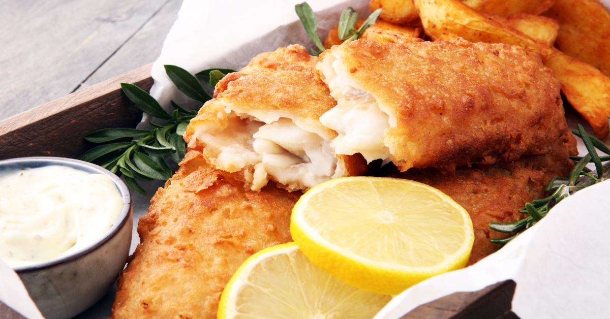 Traditional British fish and potato chips served with creamy sauce and lemon in a wooden dish.