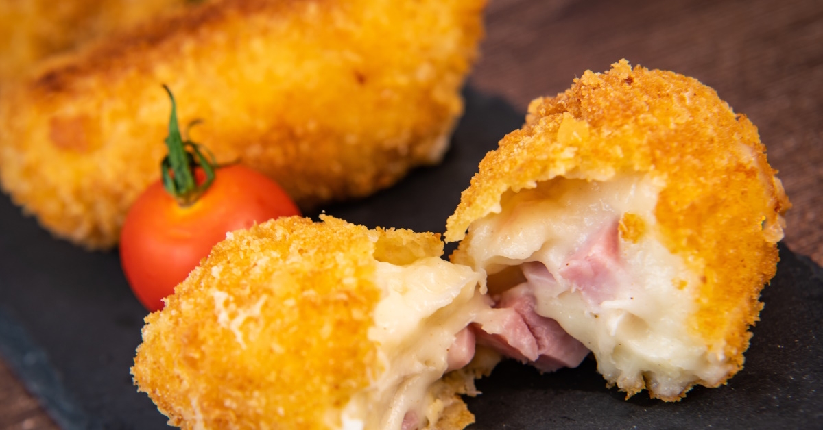 Traditional Spanish croquettes filled with cheese made at home, presented on a wooden table with a black napkin.