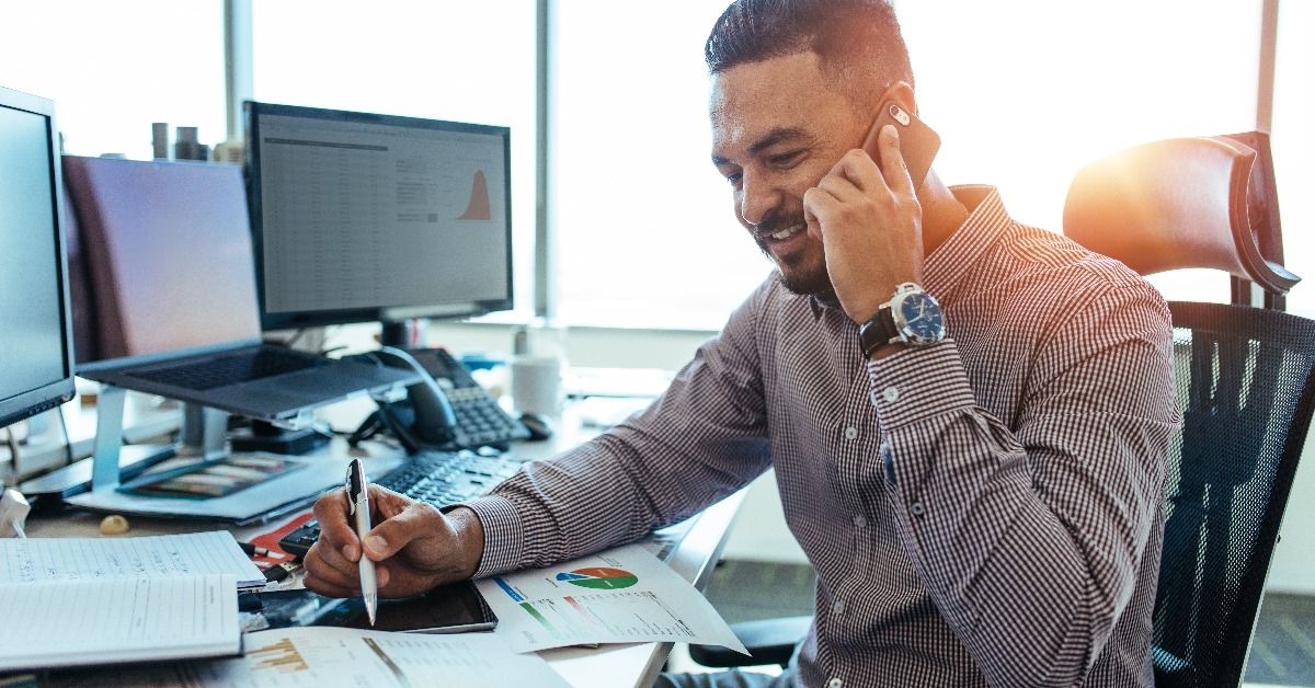 An entrepreneur is reviewing documents containing statistical data and discussing them with a colleague over the phone.