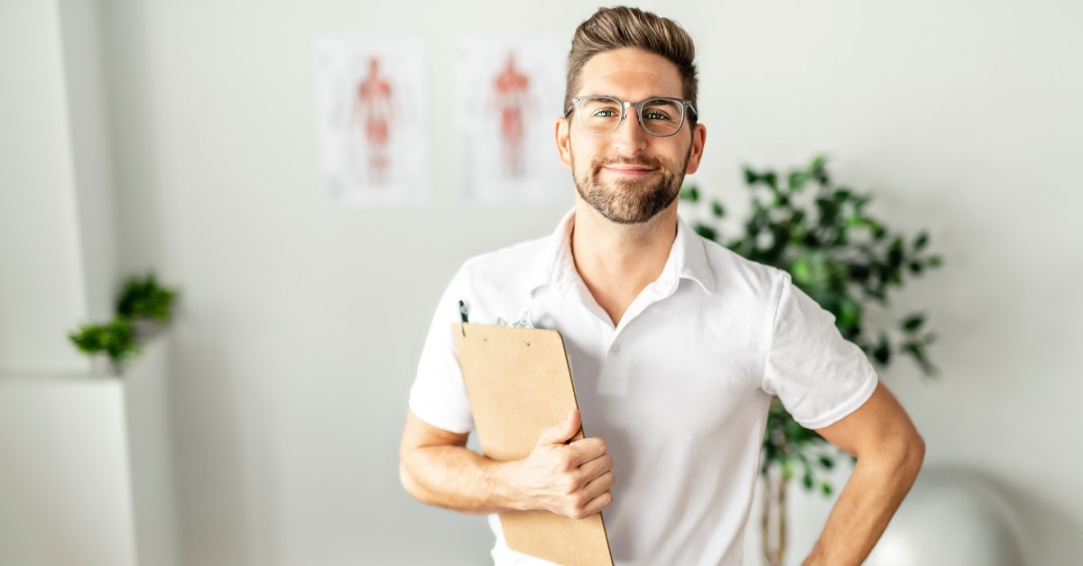 A male physiotherapist, looking professional in his white shirt, is seen standing with files at the clinic in this picture.