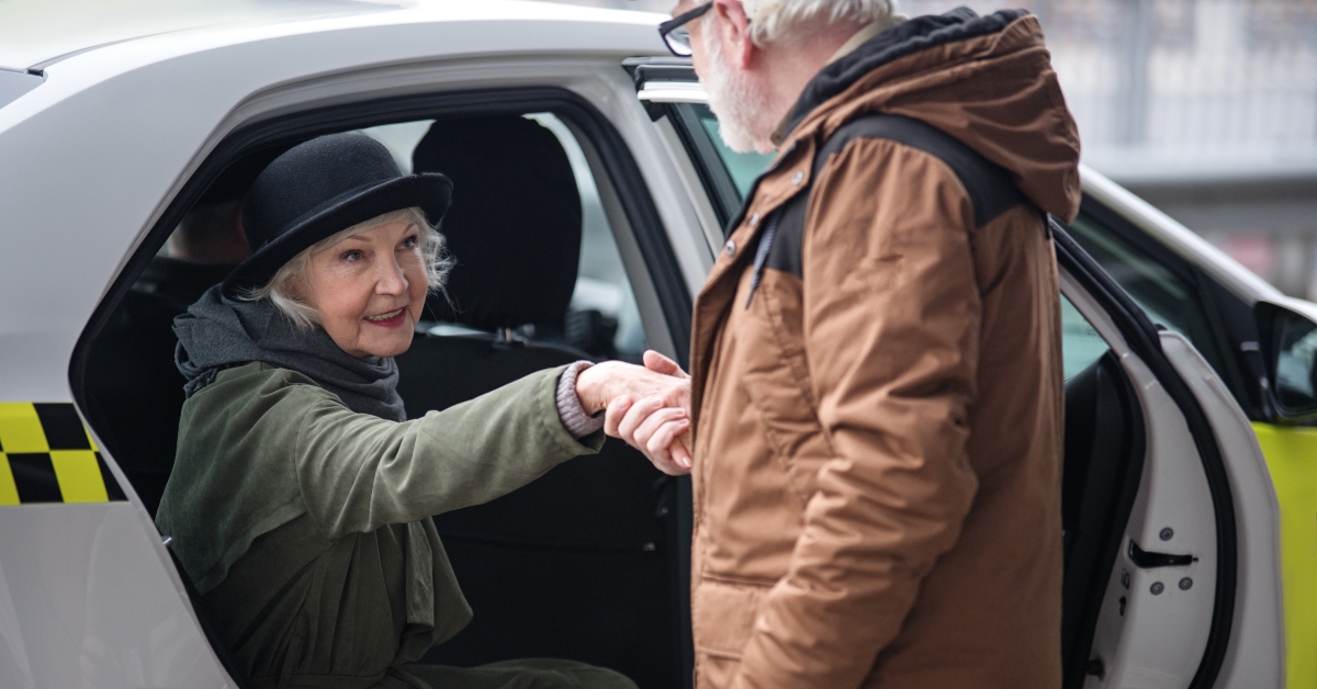 old man is helping elegant senior woman to get out of taxi