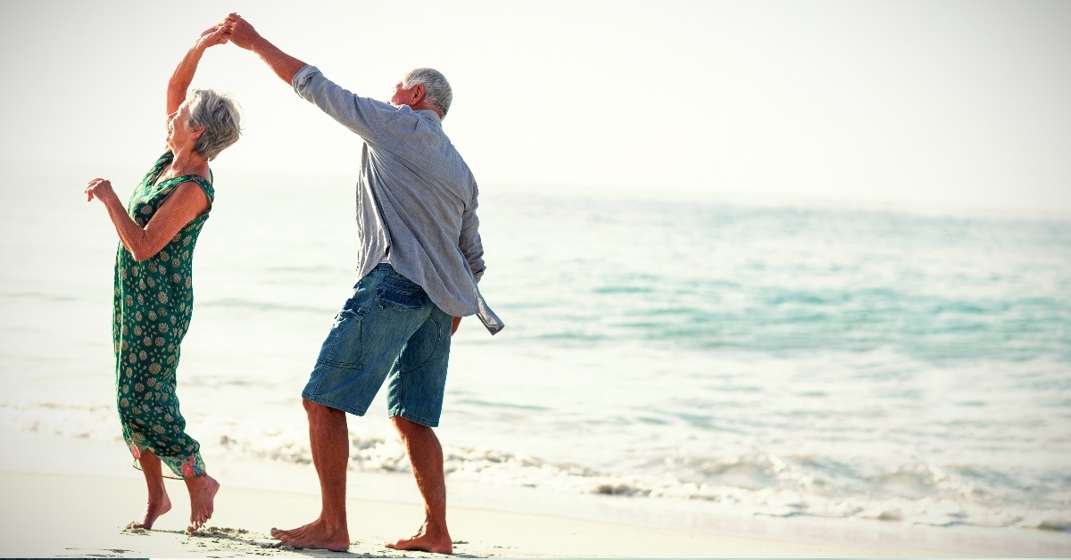 happy senior couple dancing on beach