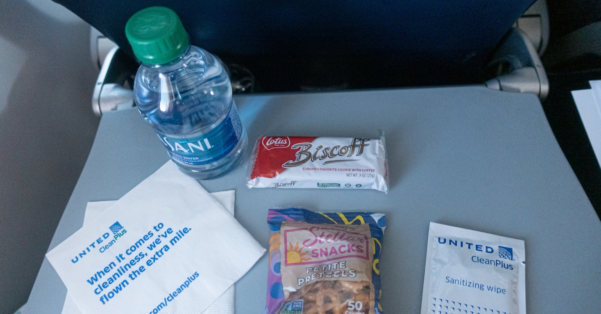 A water bottle, pretzels, and cookies on an airplane tray table