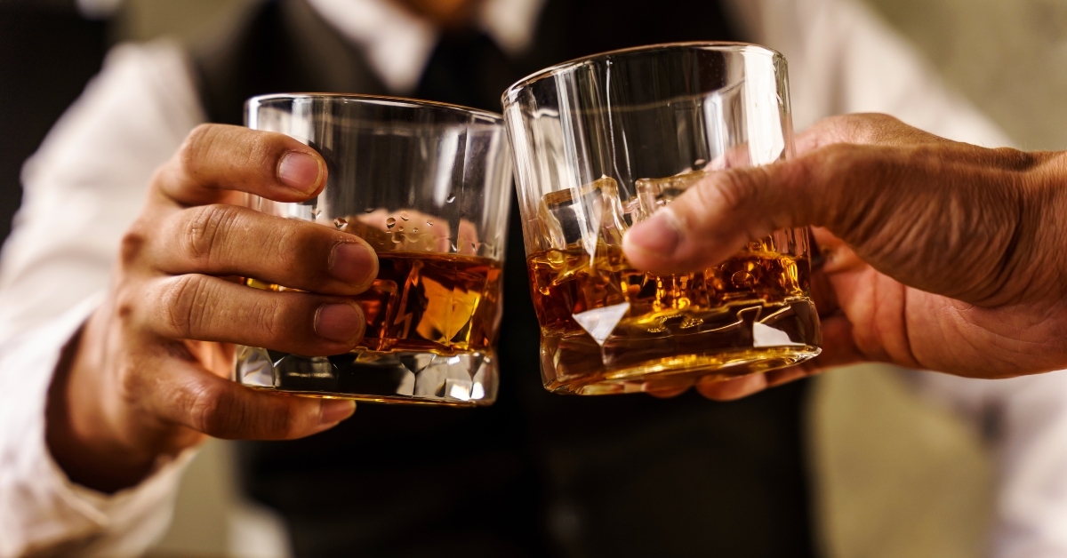 Hands clink glasses of whiskey