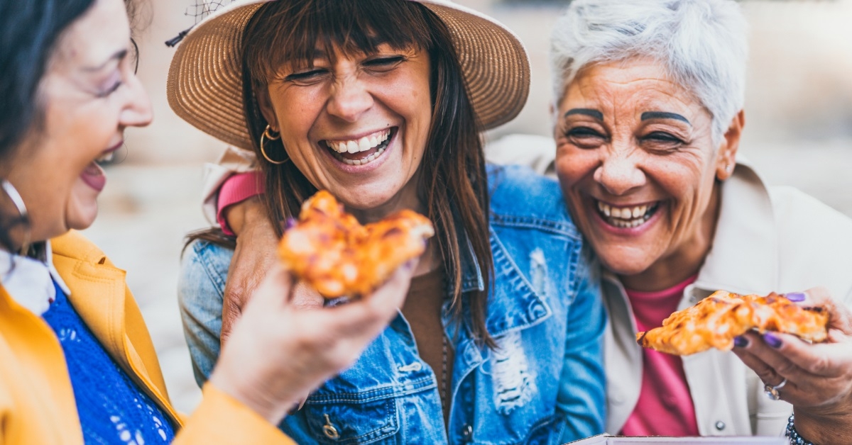 senior female friends eating pizza outdoors