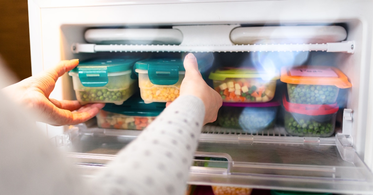 Lady placing pea and corn containers in the freezer.