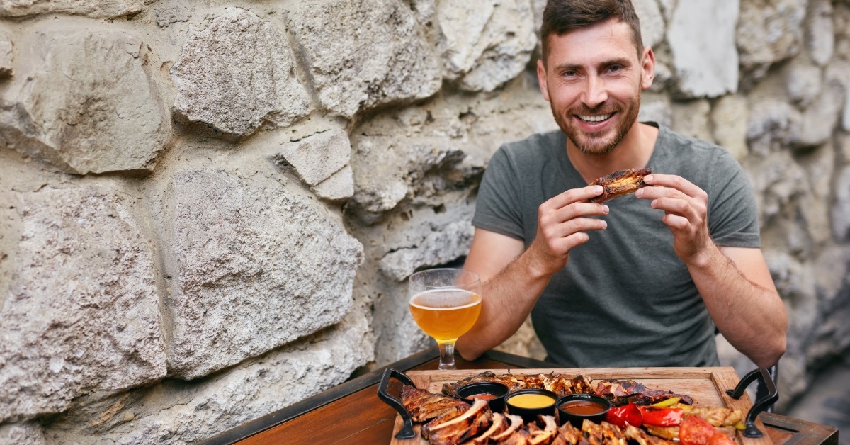 man eating barbecue meat with beer