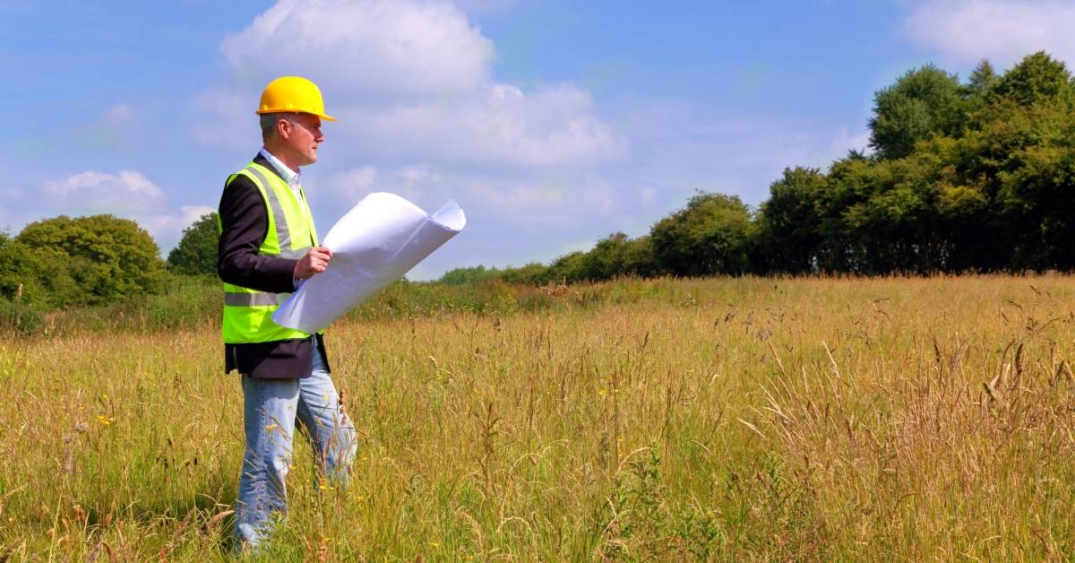 An architect in construction gear surving a new building plot.