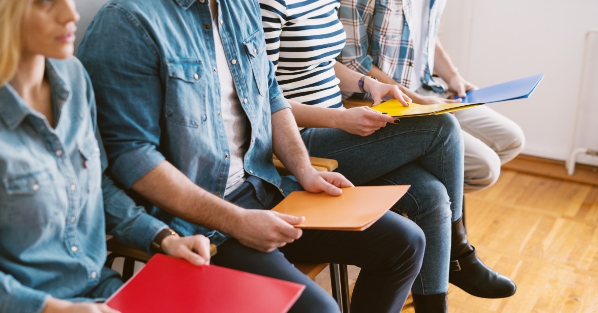 Individuals seated in chairs with portfolios prior to job interview.