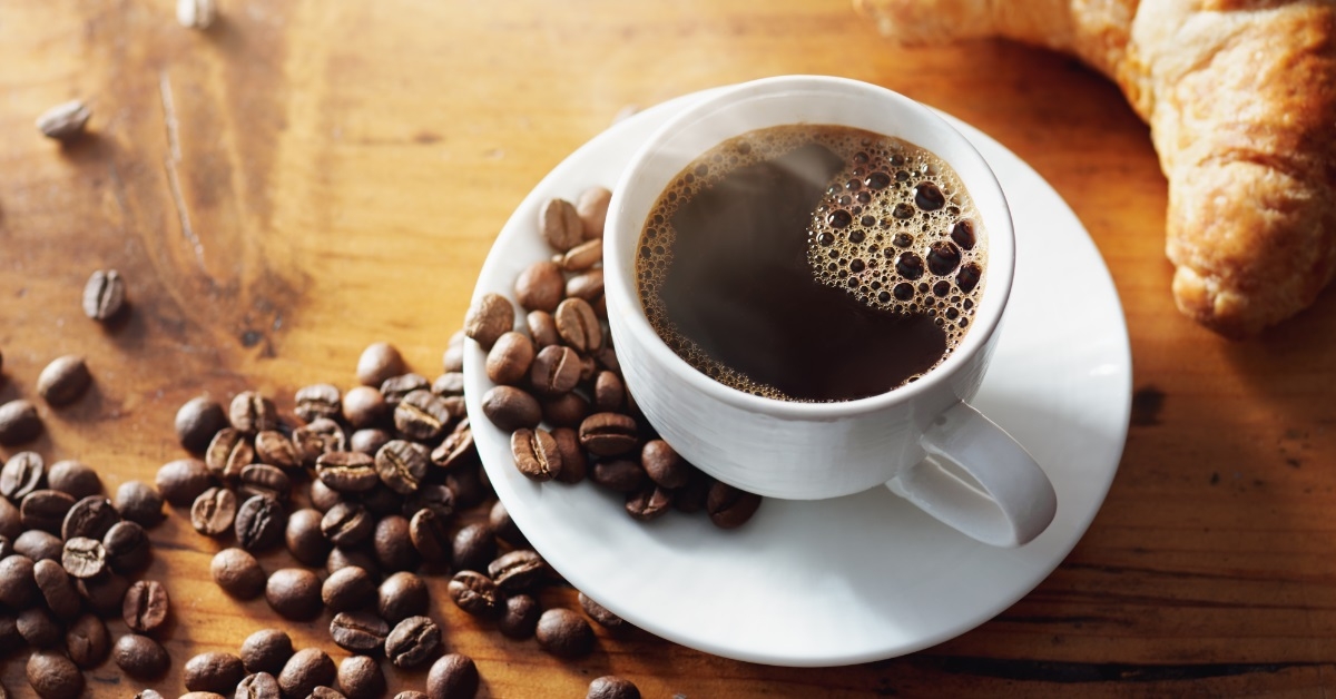 black coffee cup besides coffee beans