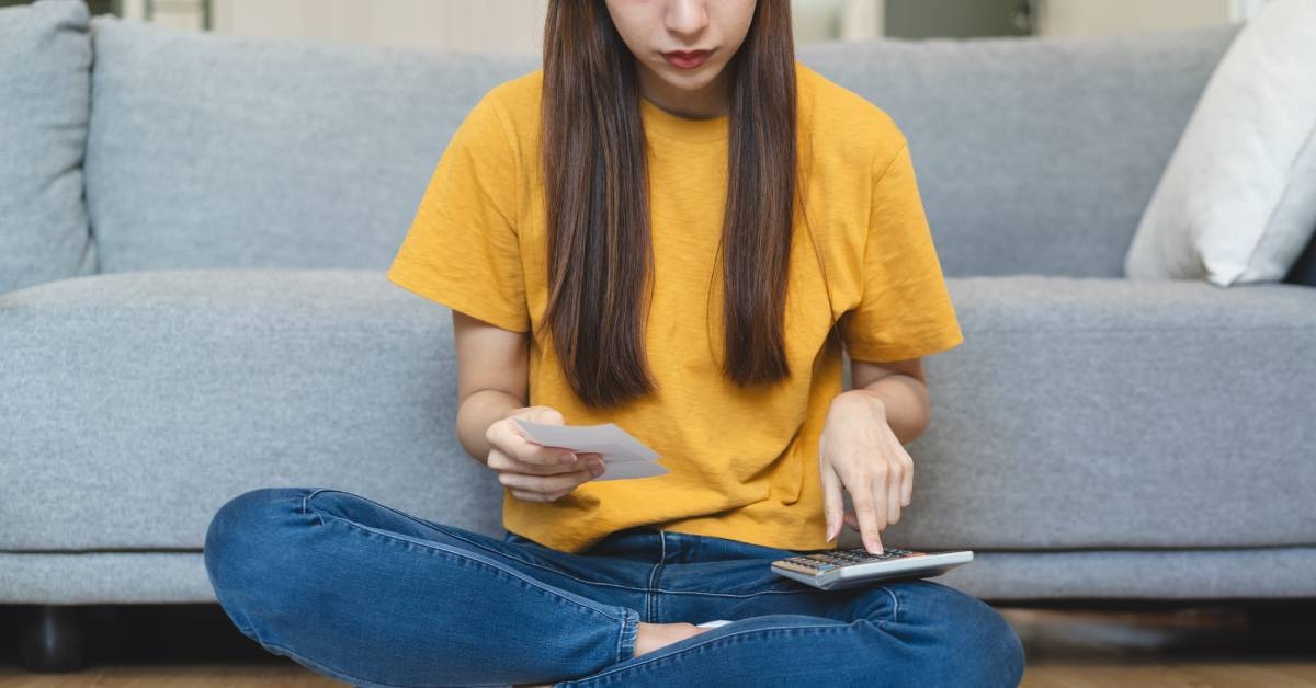 young woman using calculator calculating monthly expense from invoice receipt for manage personal finance and mortgage loan on the floor at home