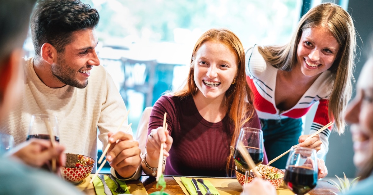 happy friends eating sushi at restaurant
