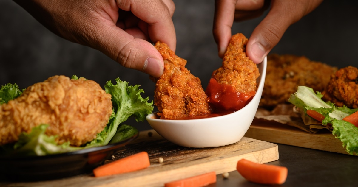 hand dipping fried chicken in ketchup