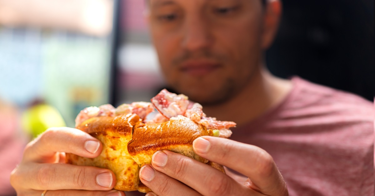 man holding lobster roll sandwich