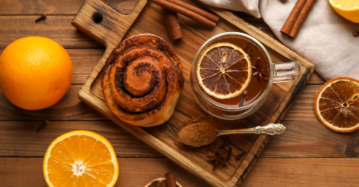 Glass cup of orange tea with cinnamon roll on wooden background