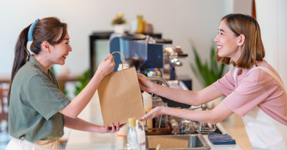 Smiling female cashier preparing takeaway order to customer.