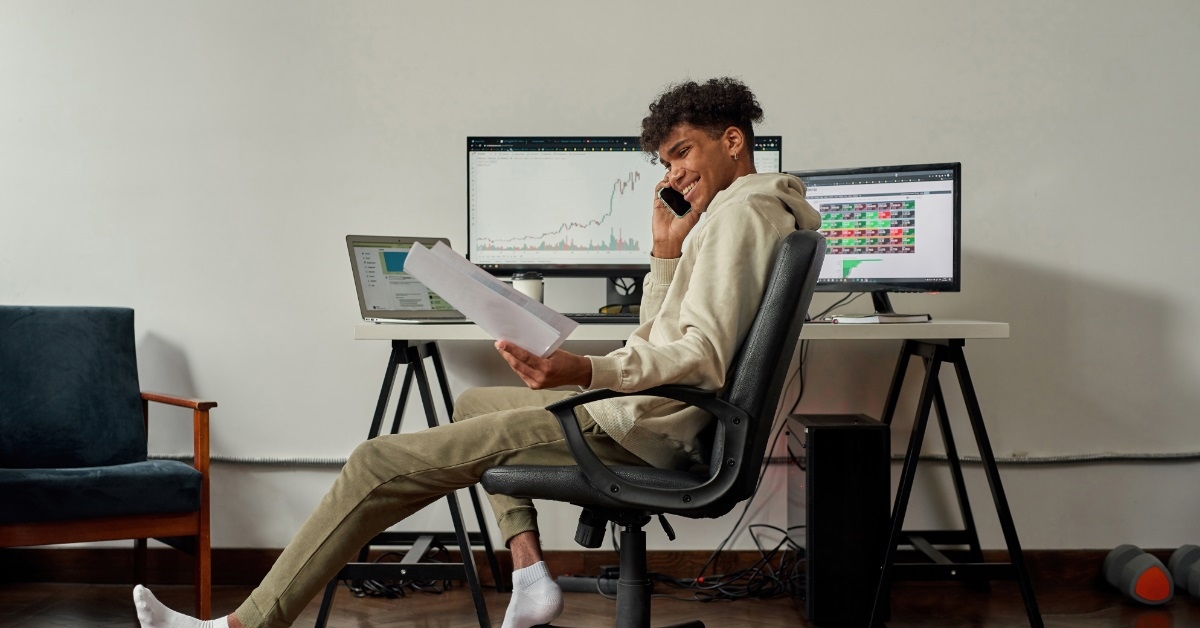 young male trader holding papers while talking on the phone