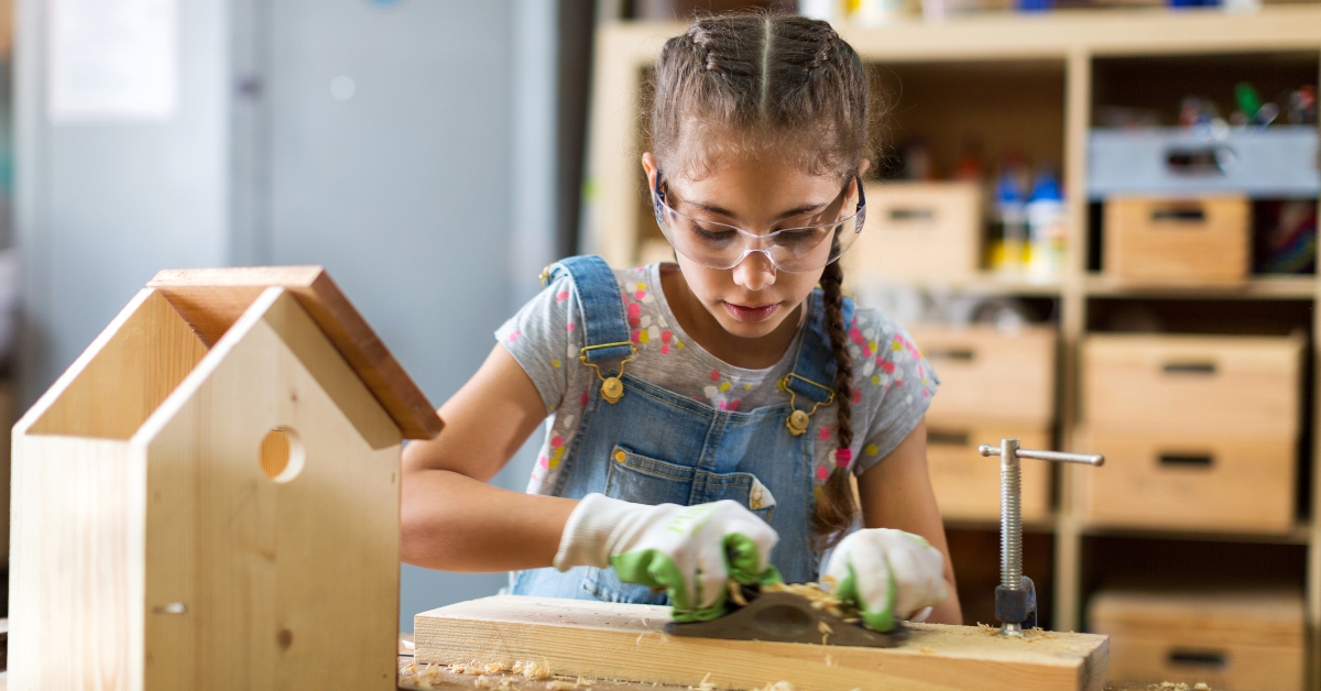 girl building birdhouse in garage