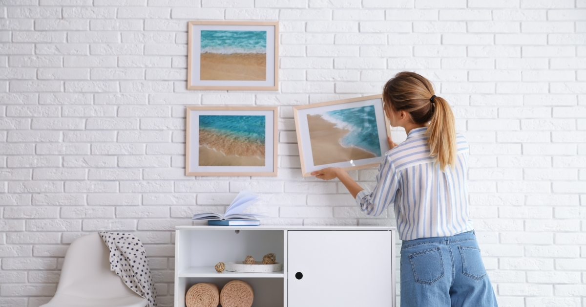 woman hanging picture on white brick wall