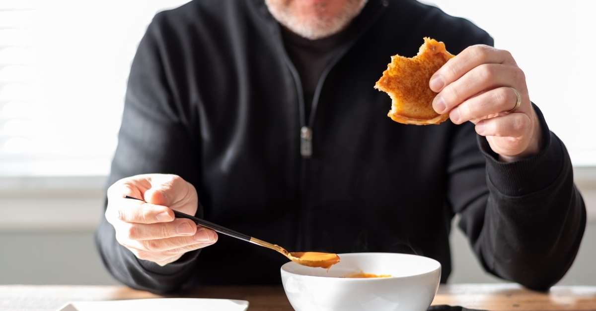 senior man eating tomato soup with bread