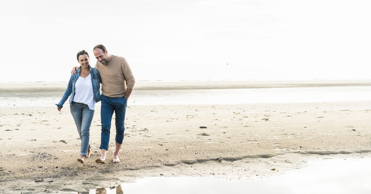 couple walking at beach against sky during sunset