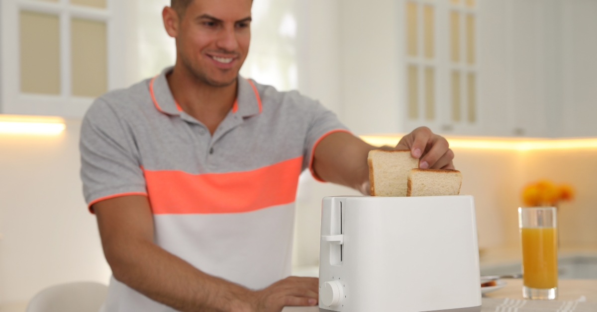 Man using toaster at table in kitchen