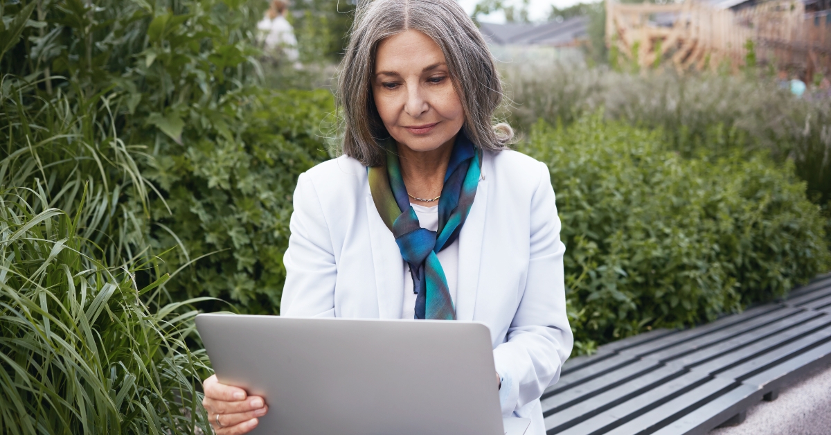women sitting on bench among green plants with portable computer