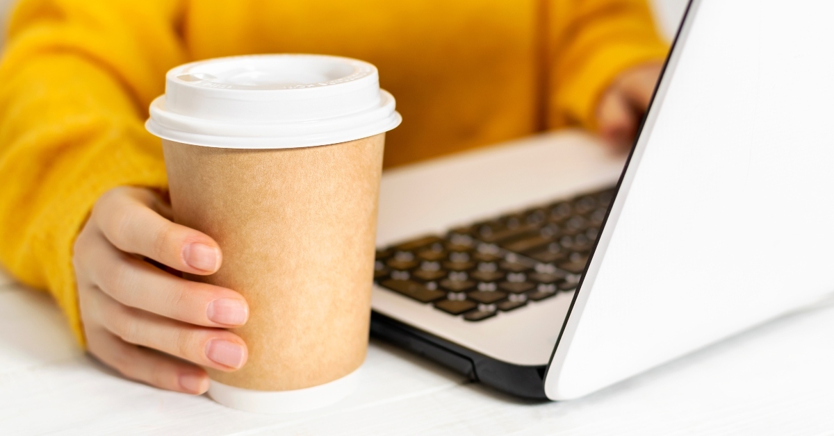 female works using a laptop and holds cup