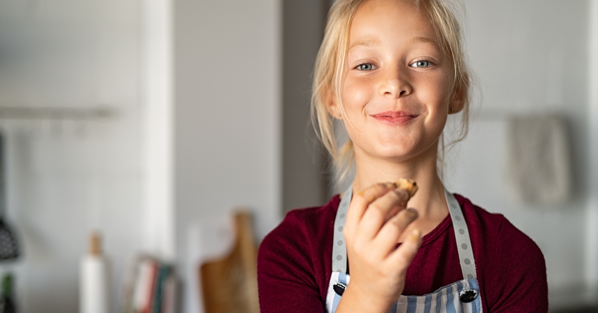 girl in apron eating handmade cookie