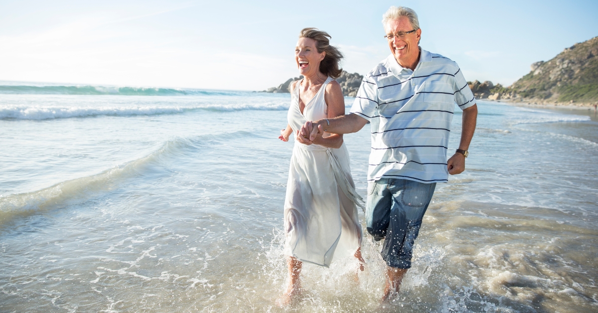 Older couple playing in waves on beach