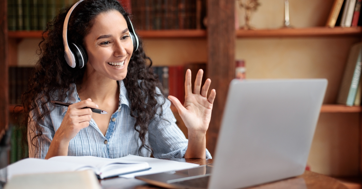 woman sitting at desk waving to webcam