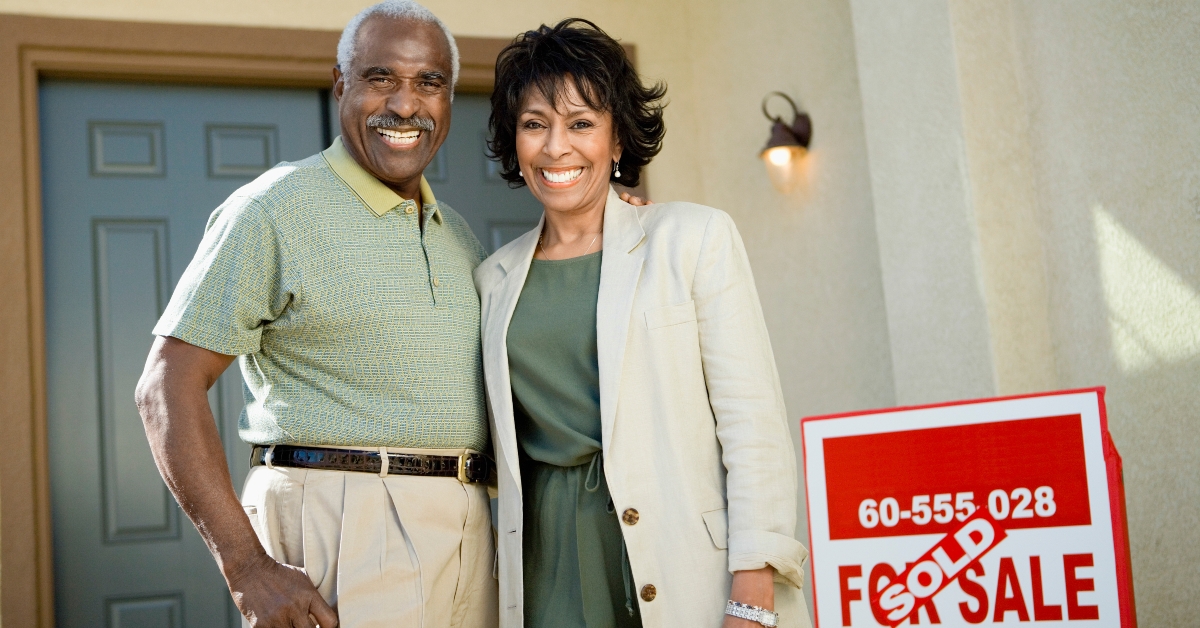 couple standing by sold real estate sign