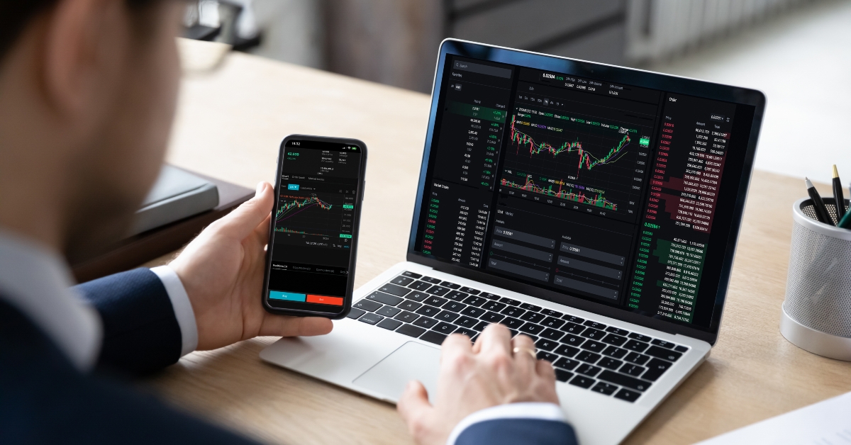 male trader sits at desk hold smart phone