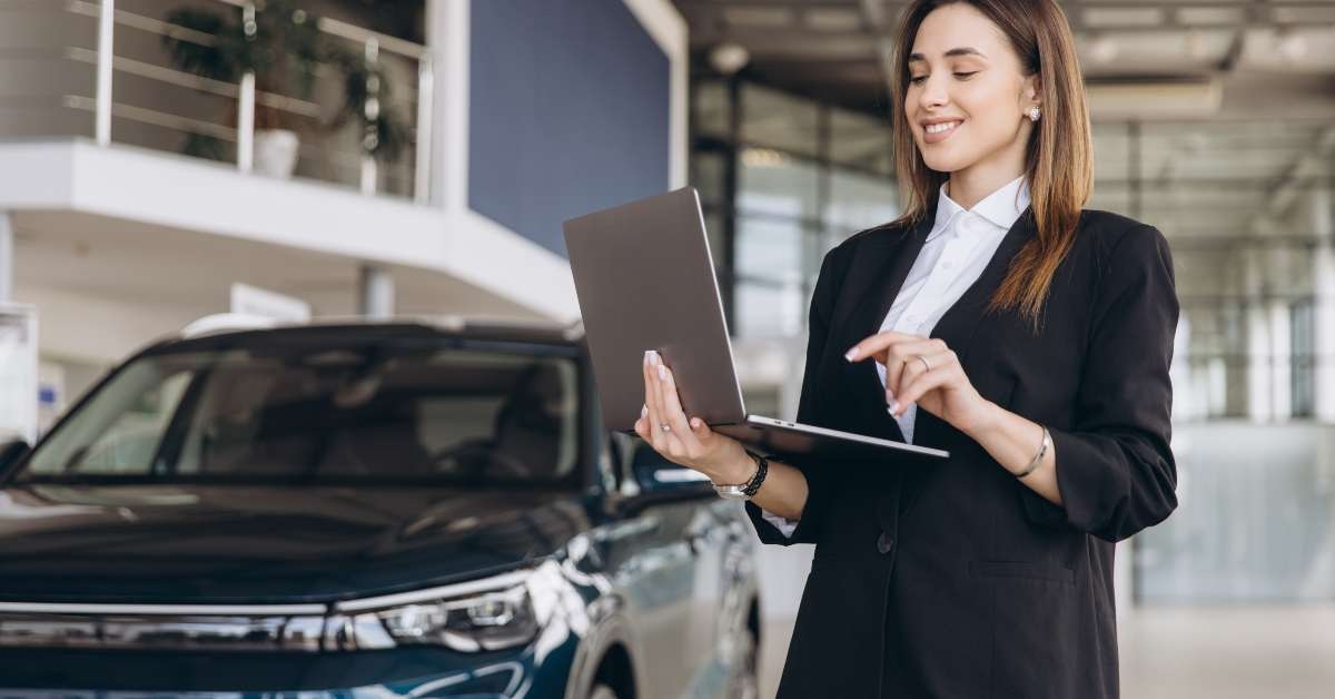 saleswoman working on laptop in car dealership