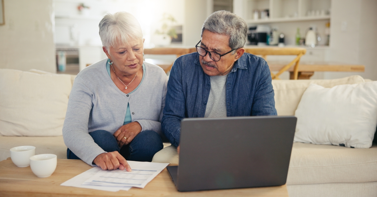 elderly couple using laptop with documents