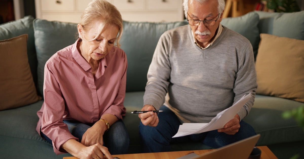 senior couple sit on a sofa calculating bills