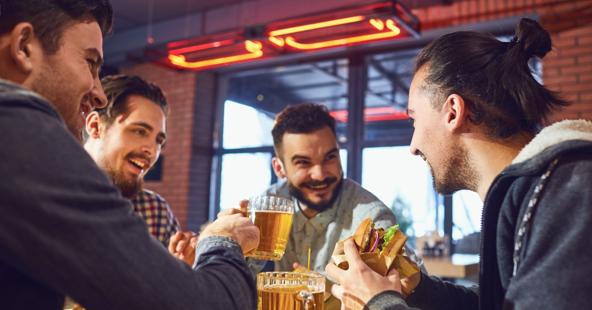 Happy friends eat burgers, drink beer in a bar