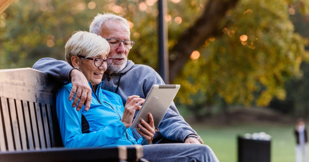 Retired couple on park bench looking at tablet