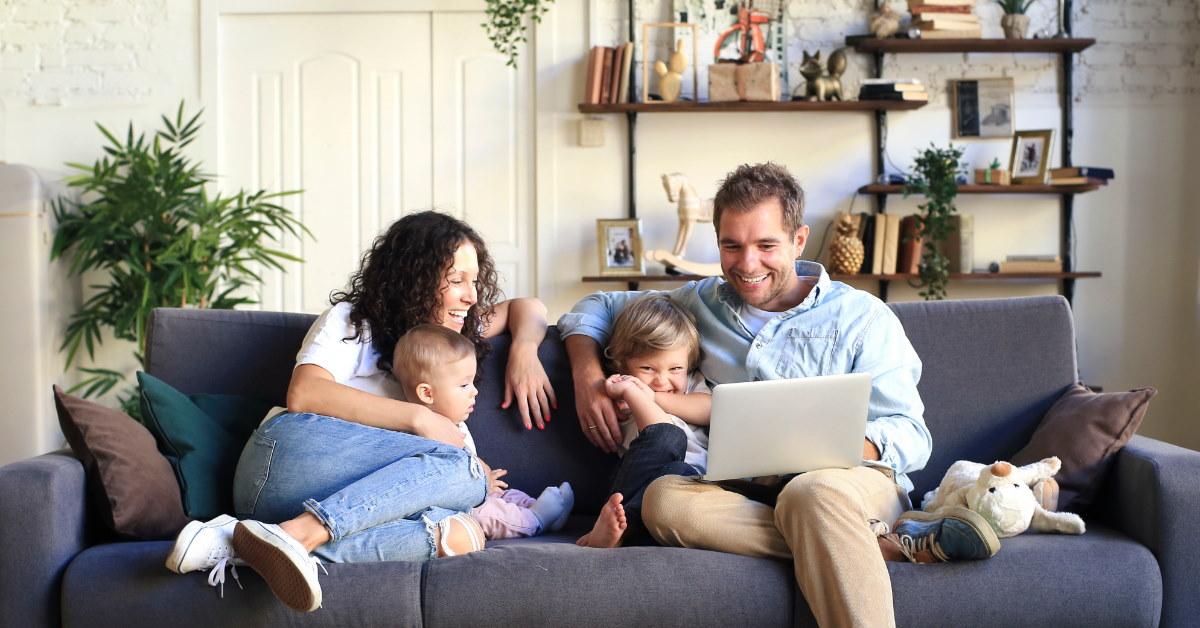 happy family sitting with kids in couch using laptop at home