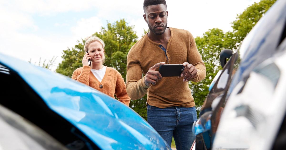 african american man taking picture of car after accident with female motorist talking on smartphone in background