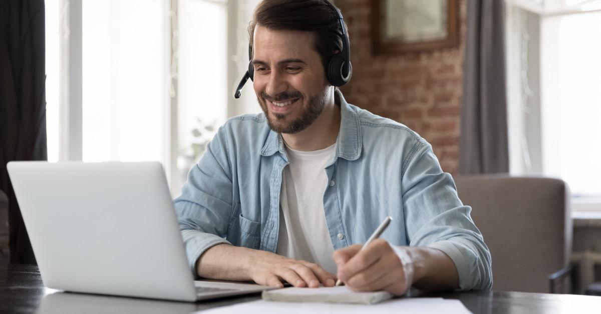 man sitting at table using laptop for work while wearing headset