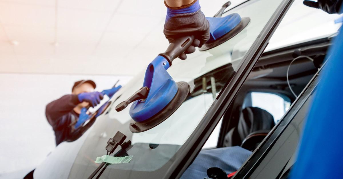 two mechanics changing windshield of car in automobile workshop