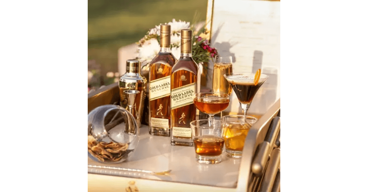 Johnnie Walker Gold Label bottle and cocktails on a table under the sun