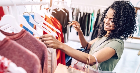Happy woman exploring rack with hangers in clothes store