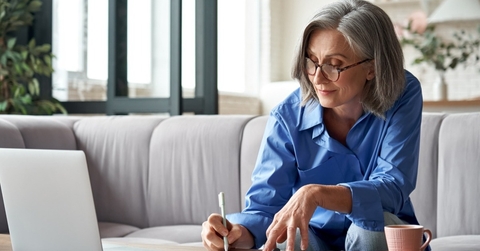 Woman in her fifties at computer writing down notes 