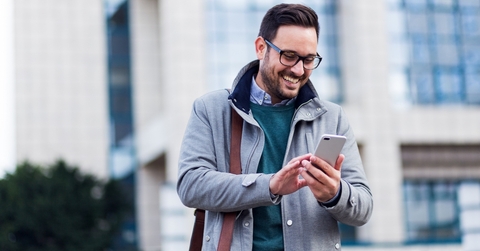 A smiling man outside wearing a coat and looking at his phone.